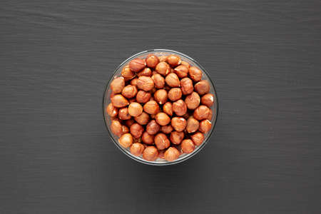 Unshelled Hazelnut in a Bowl on a black background, top view. Flat lay, overhead, from above.