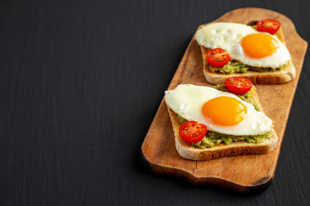 Homemade Healthy Egg, Avocado and Tomato Toast on a rustic wooden board, side view. copyspace.