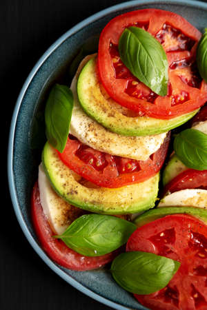 Homemade Organic Avocado Caprese Salad on a Plate on a black background, top view. Flat lay,...