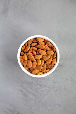 Raw brown almonds in a bowl on a gray background, top view. Flat lay, overhead, from above.の写真素材