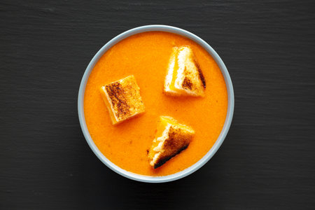 Homemade Tomato Soup with Grilled Cheese Croutons on a black background, top view. Flat lay,...