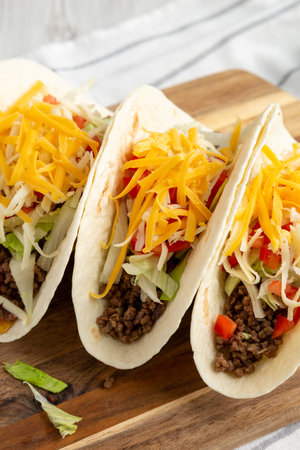 Homemade American Beef Tacos with lettuce, tomato and cheese on a wooden board, side view. close-up.