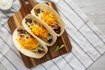 Homemade American Beef Tacos with lettuce, tomato and cheese on a wooden board, top view. Flat lay, overhead, from above. Space for text.の写真素材