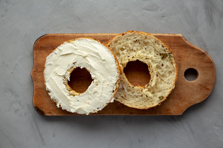 Homemade Whole Grain Bagel with Cream Cheese on a rustic wooden board, top view.の写真素材