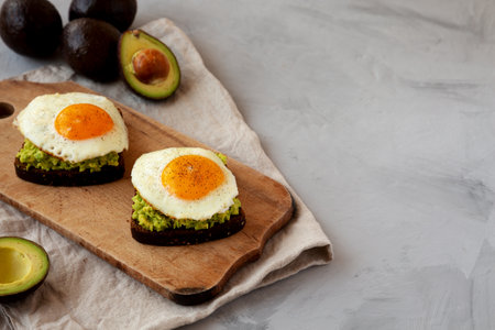 Homemade Avocado Toast with Eggs on a rustic wooden board, side view. copyspace.の写真素材