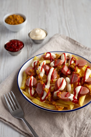 Homemade Salchipapa Fries with Ketchup, Mustard and Mayo on a Plate, side view.