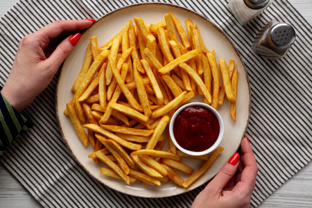 Female hands hold a plate with homemade Golden French Fries with Ketchup, top view.の写真素材
