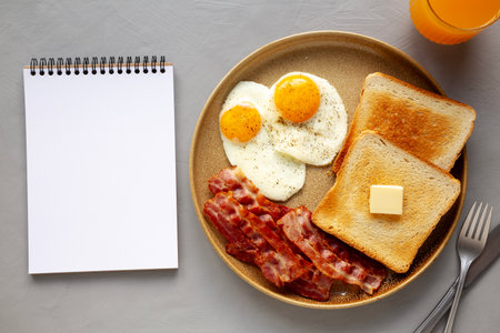 Homemade American Bacon Egg and Toast Breakfast on a Plate, blank notepad, top view.