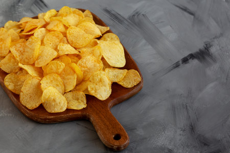 Crispy Potato Chips with Bacon Flavor on a Wooden Board, side view. Copy space.