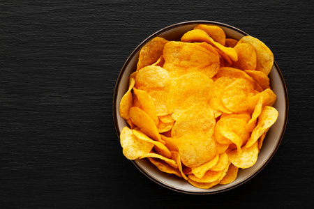 Crispy Cheese Potato Chips in a Bowl on a Black Background, top view. Copy space.