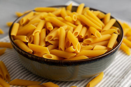 Homemade Raw Dry Penne Pasta in a Bowl, side view. Close-up.