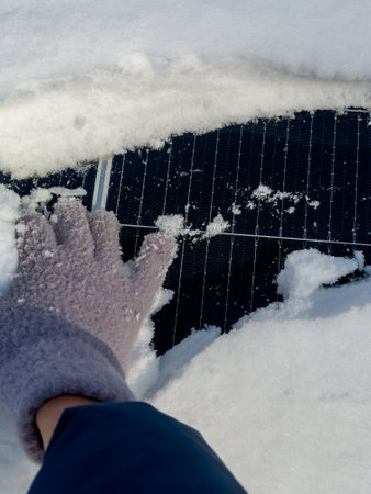 Hand clearing snow from a solar panel in winter while ensuring it remains functional for energy collectionの写真素材