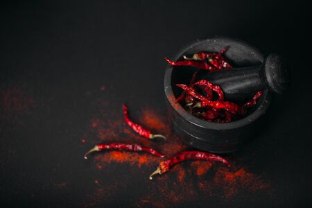 Dry red spicy peppers and powder in stone mortar. Dark photo, copy space.の写真素材