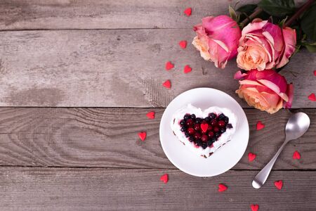 Mini romantic dessert cake for Valentine's Day with roses. Sweet cookies with cream topping and red heart for decor on wooden background. Close-up, copy space.の写真素材