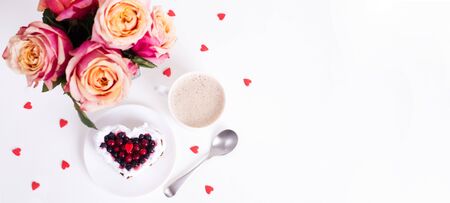 Mini romantic dessert cake for Valentine's Day with roses. Sweet cookies with cream topping and red heart for decor on white.  Flat lay. Banner. Top view, copy space.の写真素材