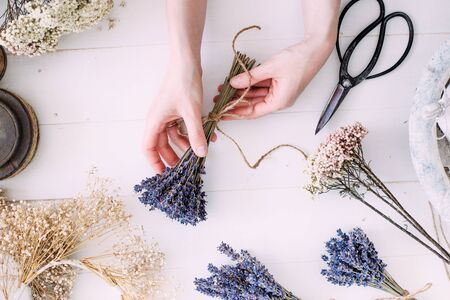 Hands of a florist woman at work. Dry compositions and bouquets of flowers and plants for the interior. White wooden rustic background. Flat lay.の写真素材