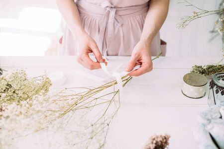 Hands of a florist woman at work. Dry compositions and bouquets of flowers and plants for the interior. White wooden rustic background.の写真素材