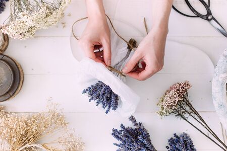 Hands of a florist woman at work. Dry compositions and bouquets of flowers and plants for the interior. White wooden rustic background. Flat lay.の写真素材