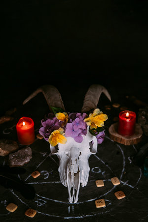 White goat scull with horns, flowers, open old book, candles on witch table. Occult, esoteric, divination and wicca concept. Halloween, Day of the dead conceptの写真素材