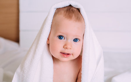 A cute baby with blue eyes wrapped in a towel as the hood looks into the camera.の写真素材