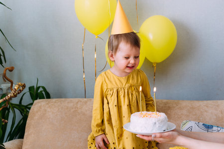 A little cute girl is celebrating her birthday at home. Cake, confetti, balloons