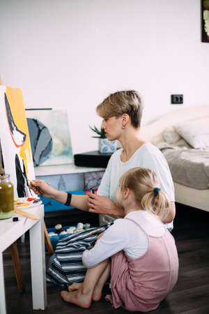 beautiful mother artist and her child paint picture at home with acrylic paints.の写真素材