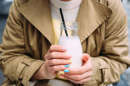 A young woman drinks a milkshake outdoors from a stylish glass jar with a strawの写真素材