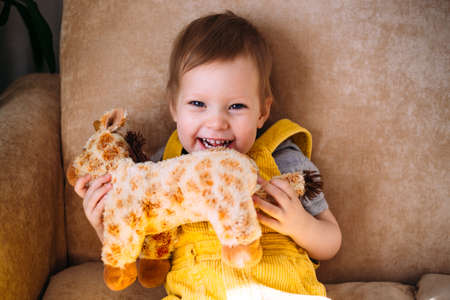 Funny little child is having fun, playing with soft toys on the couch at home.の写真素材