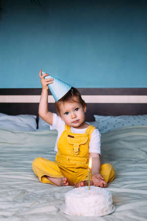 Llittle cute toddler is celebrating her birthday at home on bed with cake