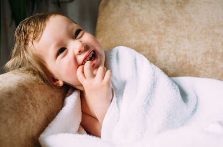 Cute baby in a big white towel. Holds fingers in the mouth.の写真素材