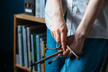 Female hands hold paint brushes. Painting a picture on an easel