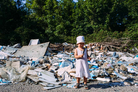 Little girl at a dump among a heap of scattered garbage in the forest.の写真素材