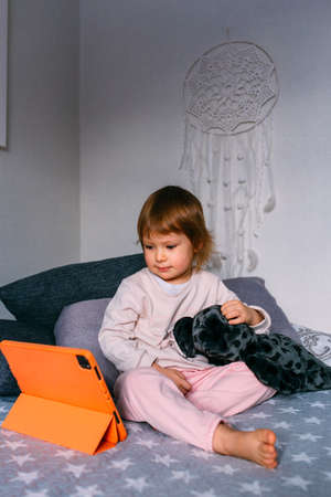 Small child watches cartoons at home on sofa on the tablet. Kid use technologyの写真素材