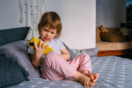 A small child at home on the couch uses a smartphoneの写真素材