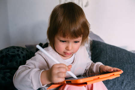 Child using technology. Toddler at home with a tablet and a pen stylus and draws
