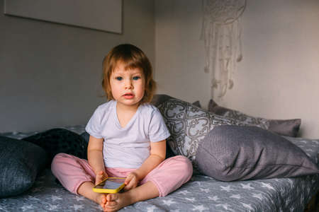 A small child at home on the couch uses a smartphoneの写真素材