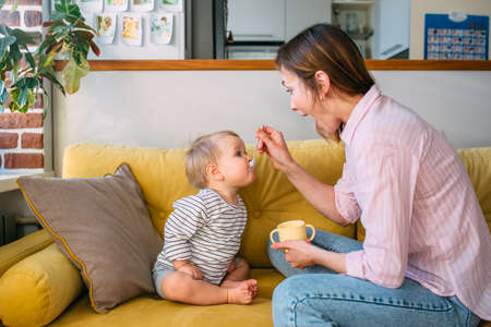 Mom feeds a small child at home with yogurt from a spoon. Family conceptの写真素材