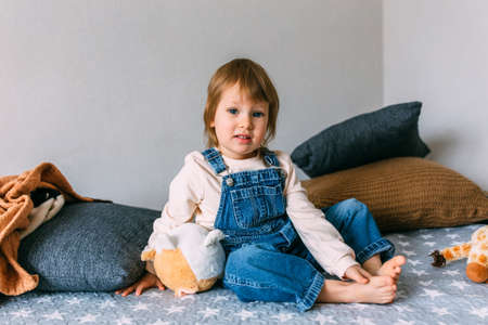 Funny little child is having fun, playing with soft toys on the couch at home.の写真素材