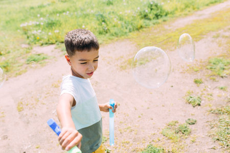Preschooler boy blows big soap bubbles in a field on a bright sunny dayの写真素材