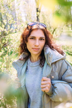 Portrait of a young brunette woman in spring in a park in outerwear.