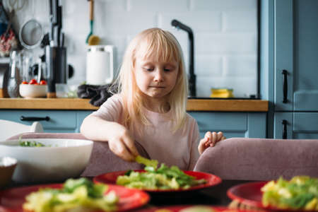 Little blonde girl is helping to prepare dinner in the kitchen.の写真素材