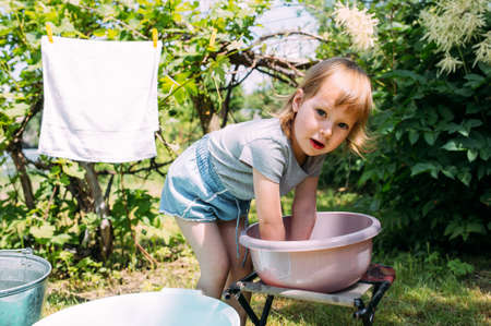 Little preschool girl helps with laundry. Child washes clothes in gardenの写真素材