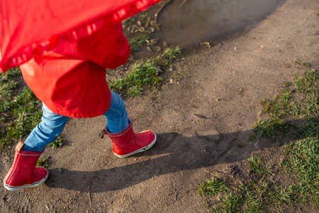Child plays with umbrella after the rain in red rubber boots and a raincoat.の写真素材