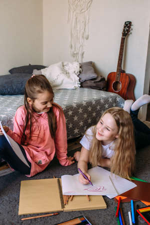 Two girls friends play at home, draw with pencils and felt-tip pens and have funの写真素材
