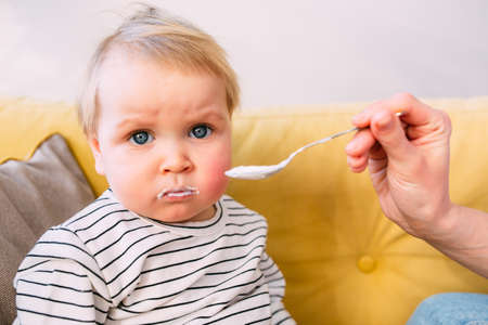 Mom feeds a small child at home with yogurt from a spoon. Family conceptの写真素材