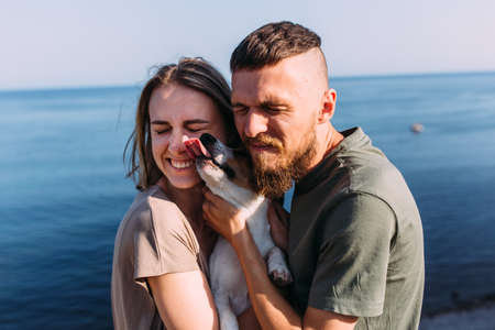 Happy couple with favourite pet. Young man and woman have walk near sea.の写真素材