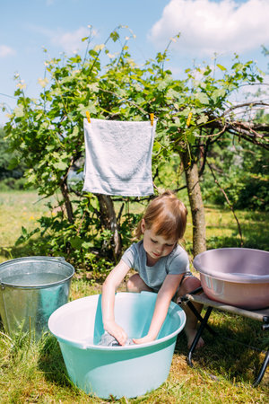 Little preschool girl helps with laundry. Child washes clothes in gardenの写真素材