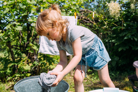Little preschool girl helps with laundry. Child washes clothes in gardenの写真素材