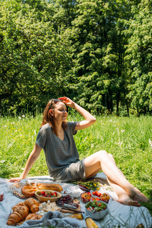 Beautiful woman on picnic. She smiles, eats strawberries and enjoys summer.の写真素材