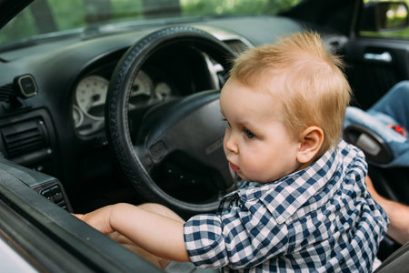 Dad shows his little son how to drive car while sitting behind wheelの写真素材